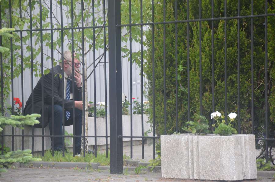 Кшиштоф Савіці неподалік від активістів, за парканом, щось конспектує і курить цигарку><span class=