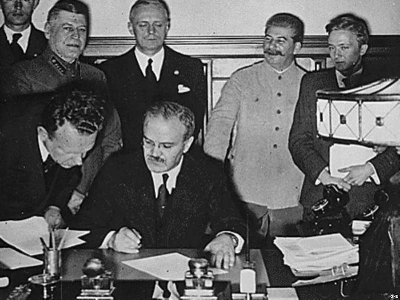 В'ячеслав Молотов ставить підпис під радянсько-німецькою угодою про ненапад, відомий, як Пакт Молотова-Ріббентропа . За ним стоять міністр закордонних справ Німеччини Йоахім фон Ріббентроп та Сталін. Кремль, 23 серпня 1939 року.